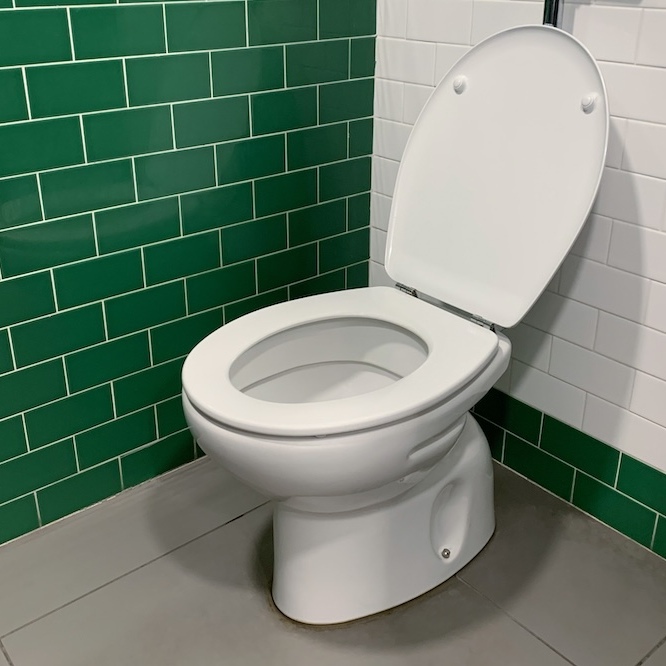 A toilet with a green tile background.